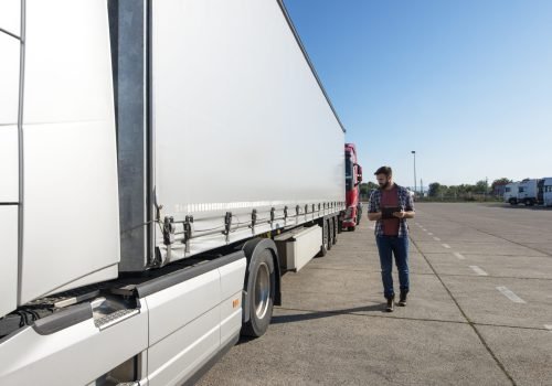 Truck driver inspecting vehicle, trailer and tires before driving.